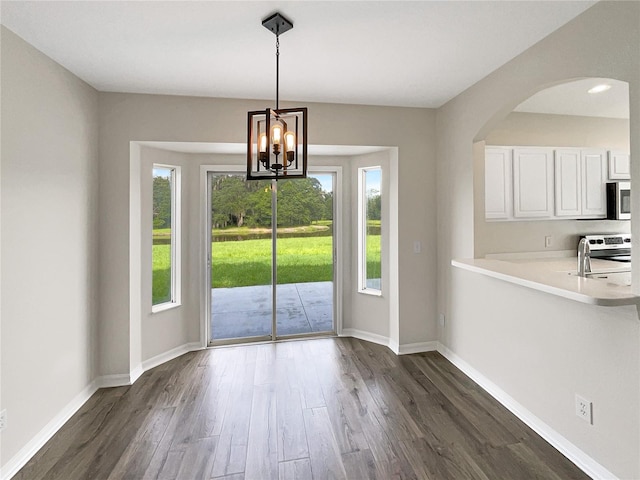 unfurnished dining area with a notable chandelier, sink, dark hardwood / wood-style flooring, and a healthy amount of sunlight