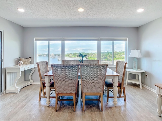 dining area featuring a textured ceiling, light wood-type flooring, and a water view