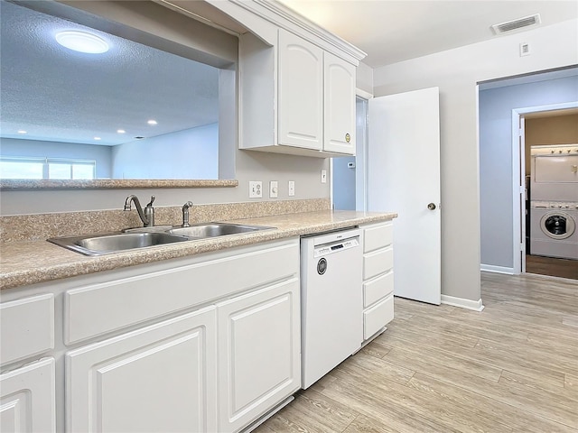 kitchen with white cabinets, white dishwasher, sink, light wood-type flooring, and stacked washer / drying machine