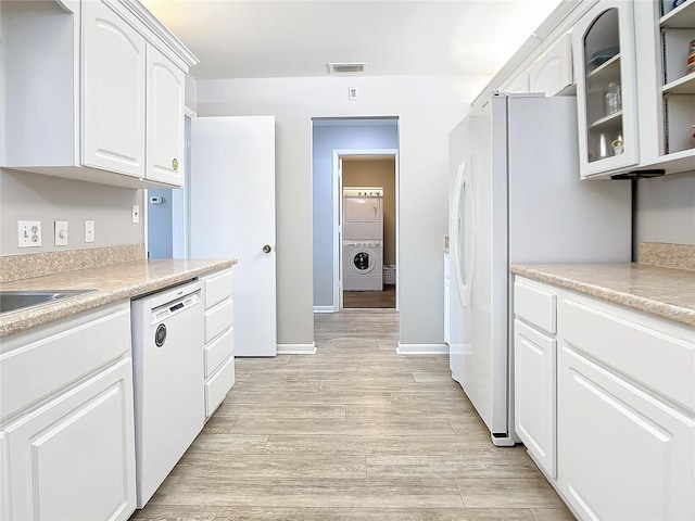 kitchen with white cabinets, light hardwood / wood-style flooring, stacked washer and dryer, and white appliances