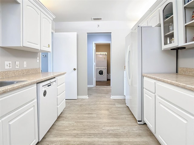 kitchen featuring stacked washer / dryer, light wood-style floors, white appliances, light countertops, and white cabinetry