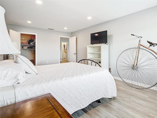 bedroom with wood finished floors, visible vents, recessed lighting, and a walk in closet