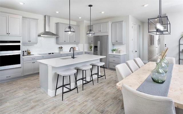 kitchen with pendant lighting, gray cabinets, stainless steel appliances, sink, and wall chimney range hood