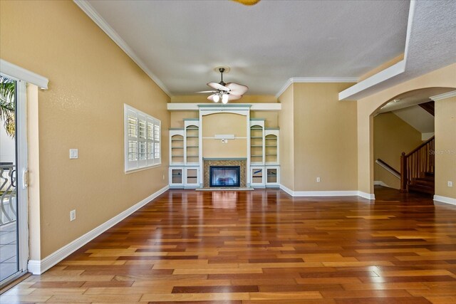 unfurnished living room with baseboards, arched walkways, a glass covered fireplace, hardwood / wood-style flooring, and crown molding