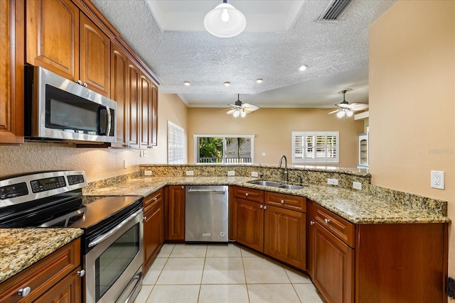 kitchen with brown cabinetry, light stone counters, a peninsula, stainless steel appliances, and a sink