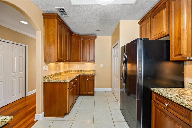 kitchen featuring light stone counters, ornamental molding, a textured ceiling, black refrigerator with ice dispenser, and light wood-type flooring