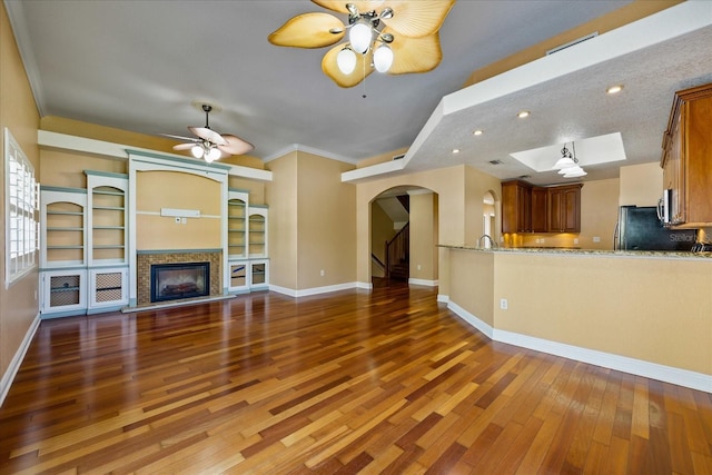 unfurnished living room featuring a fireplace, baseboards, dark wood finished floors, and a ceiling fan