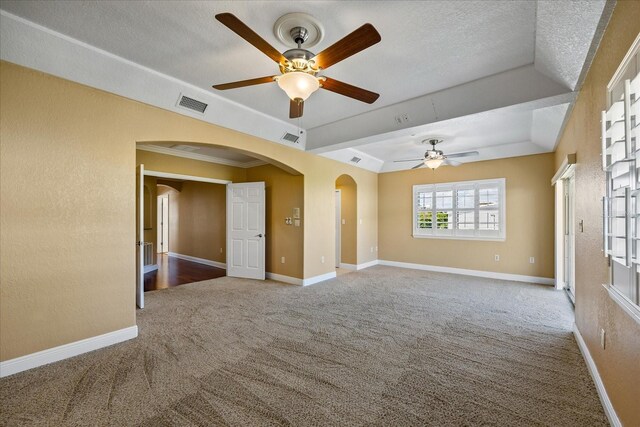 carpeted empty room with a tray ceiling, visible vents, arched walkways, and a textured ceiling