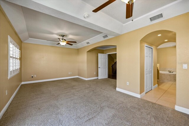 empty room featuring arched walkways, light colored carpet, visible vents, ceiling fan, and baseboards