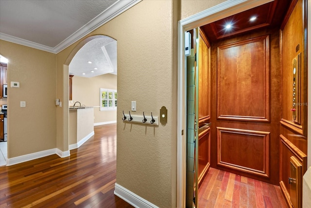 hallway with baseboards, arched walkways, elevator, ornamental molding, and wood finished floors