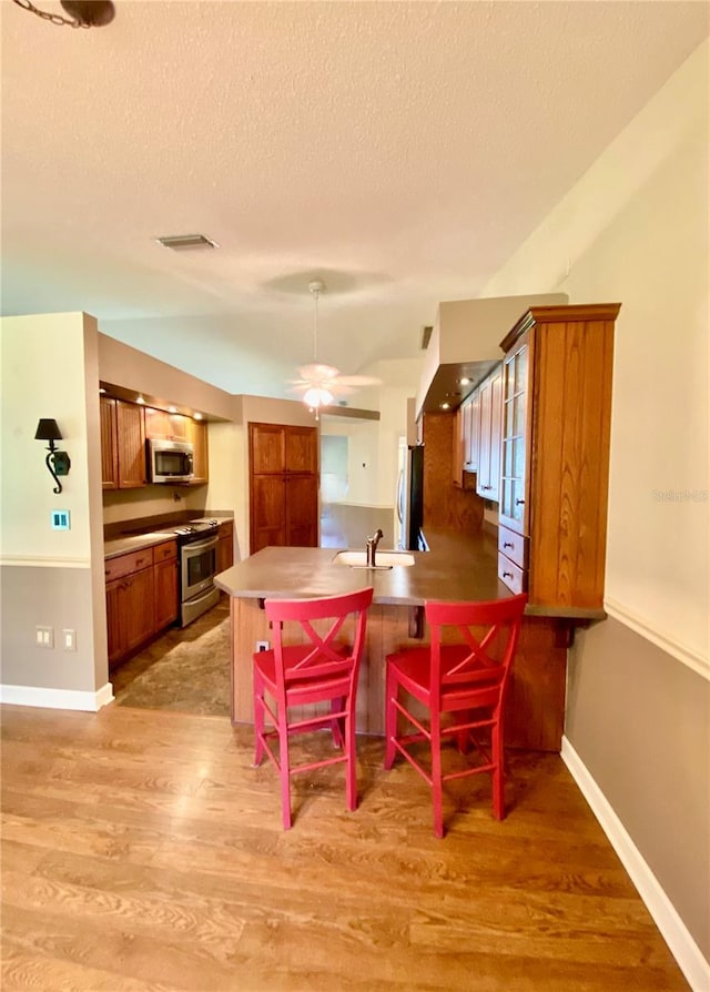 dining space featuring a textured ceiling, sink, light hardwood / wood-style flooring, and ceiling fan