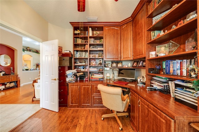 office space featuring light hardwood / wood-style flooring, built in desk, and a textured ceiling