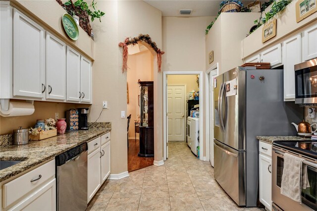 kitchen with washer / dryer, light tile patterned flooring, white cabinetry, appliances with stainless steel finishes, and light stone countertops