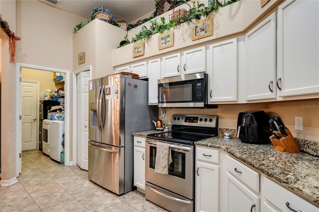 kitchen with washer / clothes dryer, light tile patterned flooring, white cabinets, light stone countertops, and stainless steel appliances