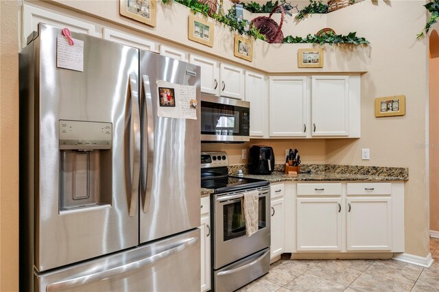 kitchen with dark stone countertops, white cabinets, appliances with stainless steel finishes, and light tile patterned floors