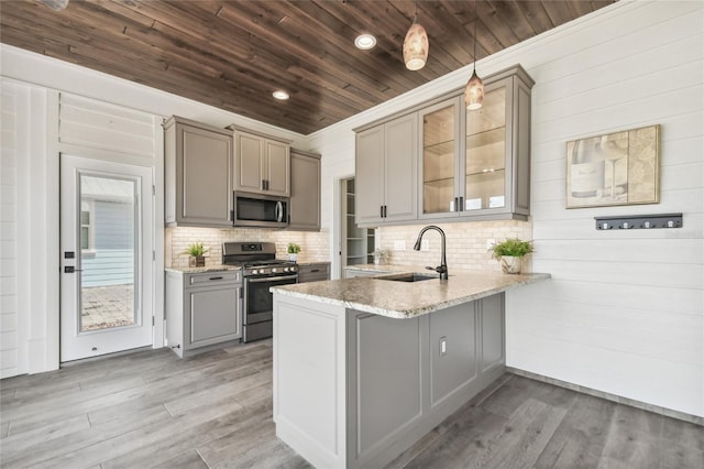 kitchen featuring pendant lighting, sink, kitchen peninsula, appliances with stainless steel finishes, and light hardwood / wood-style floors