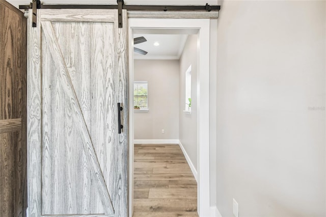 hall with wood-type flooring, ornamental molding, and a barn door