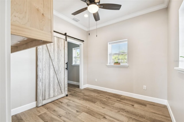 empty room featuring ceiling fan, light hardwood / wood-style floors, crown molding, and a barn door