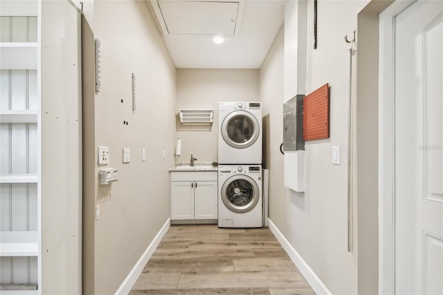 clothes washing area with cabinets, light hardwood / wood-style flooring, stacked washer / dryer, and sink