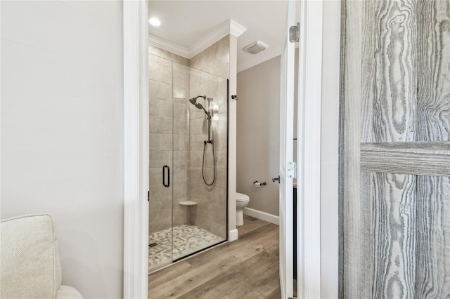 bathroom with wood-type flooring, crown molding, a shower with shower door, and toilet