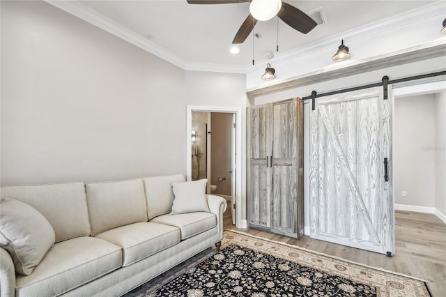 living room featuring ornamental molding, light hardwood / wood-style floors, ceiling fan, and a barn door