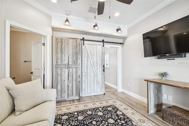 living room featuring light hardwood / wood-style flooring, ceiling fan, ornamental molding, and a barn door