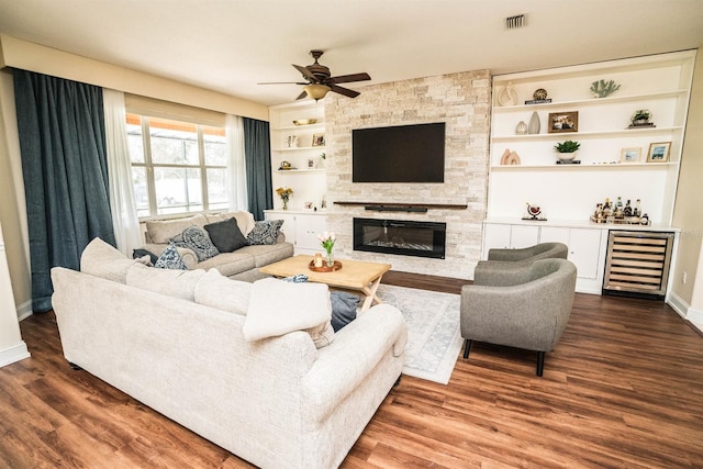 living room with dark hardwood / wood-style floors, beverage cooler, built in shelves, a stone fireplace, and ceiling fan