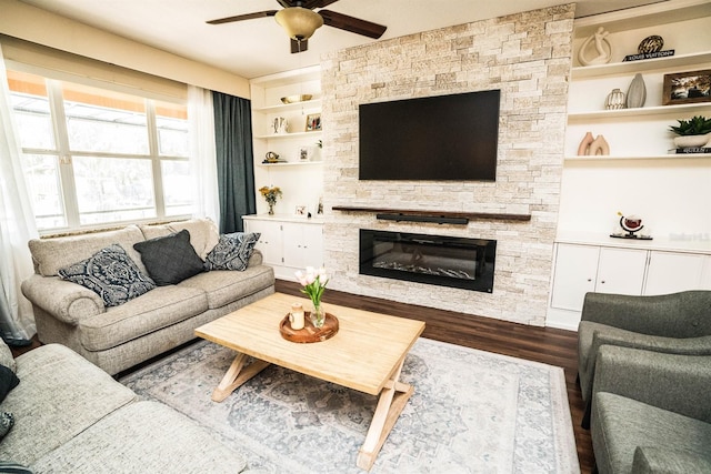 living room featuring a stone fireplace, dark hardwood / wood-style flooring, ceiling fan, and built in shelves