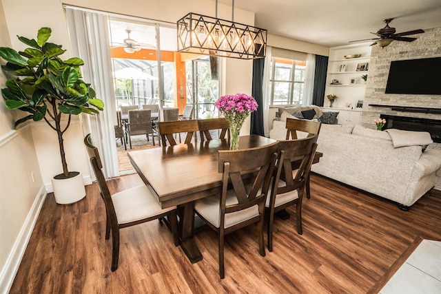 dining space with built in shelves, ceiling fan, hardwood / wood-style flooring, and a stone fireplace