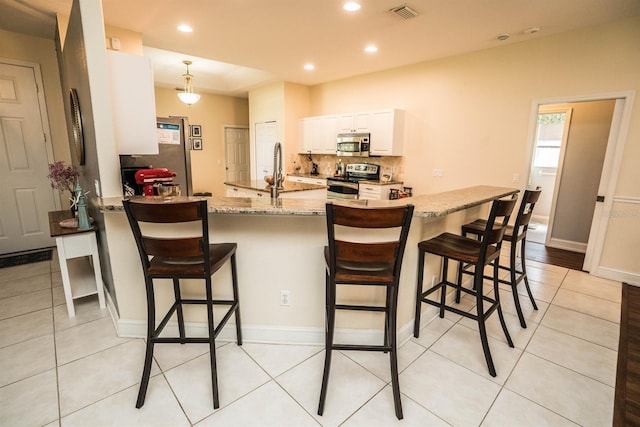 kitchen featuring a kitchen breakfast bar, light stone counters, white cabinets, stainless steel appliances, and decorative light fixtures