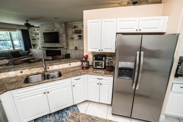 kitchen with dark stone counters, stainless steel fridge with ice dispenser, sink, white cabinets, and a fireplace