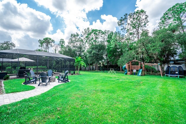 view of yard featuring a trampoline, a patio area, an outdoor fire pit, a playground, and glass enclosure