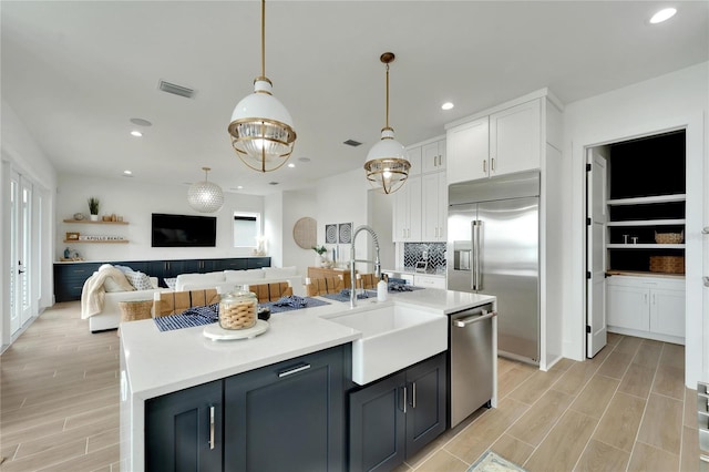 kitchen with pendant lighting, an island with sink, white cabinetry, stainless steel appliances, and light wood-type flooring