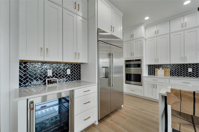 kitchen with light hardwood / wood-style floors, wine cooler, tasteful backsplash, white cabinets, and stainless steel appliances