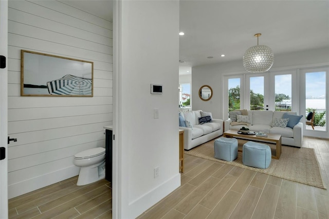 living room with french doors, wooden walls, and light hardwood / wood-style floors