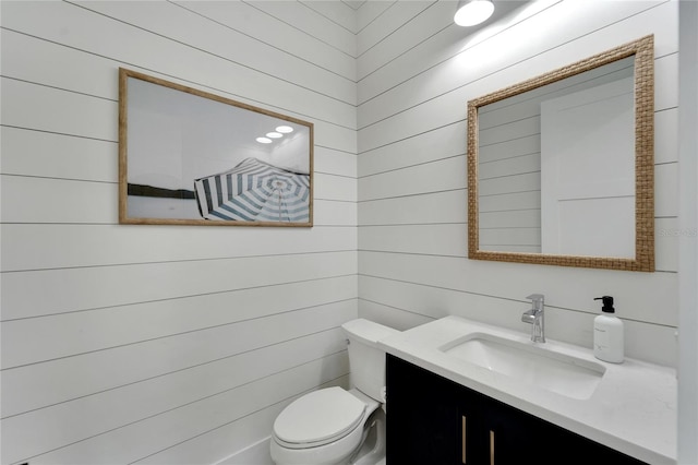 bathroom with vanity, wood walls, and toilet