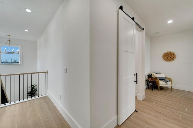 hallway with a notable chandelier, light hardwood / wood-style floors, and a barn door