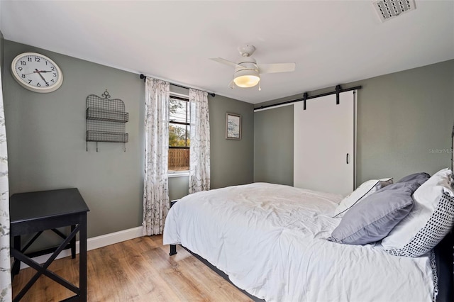 bedroom with hardwood / wood-style flooring, ceiling fan, and a barn door