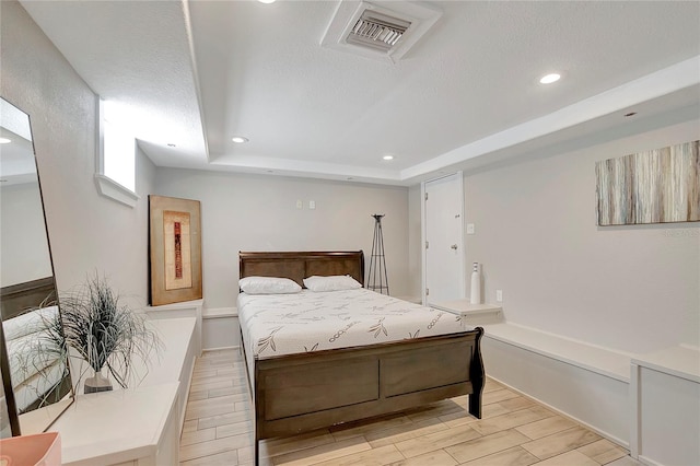 bedroom featuring a textured ceiling, a raised ceiling, and light hardwood / wood-style flooring