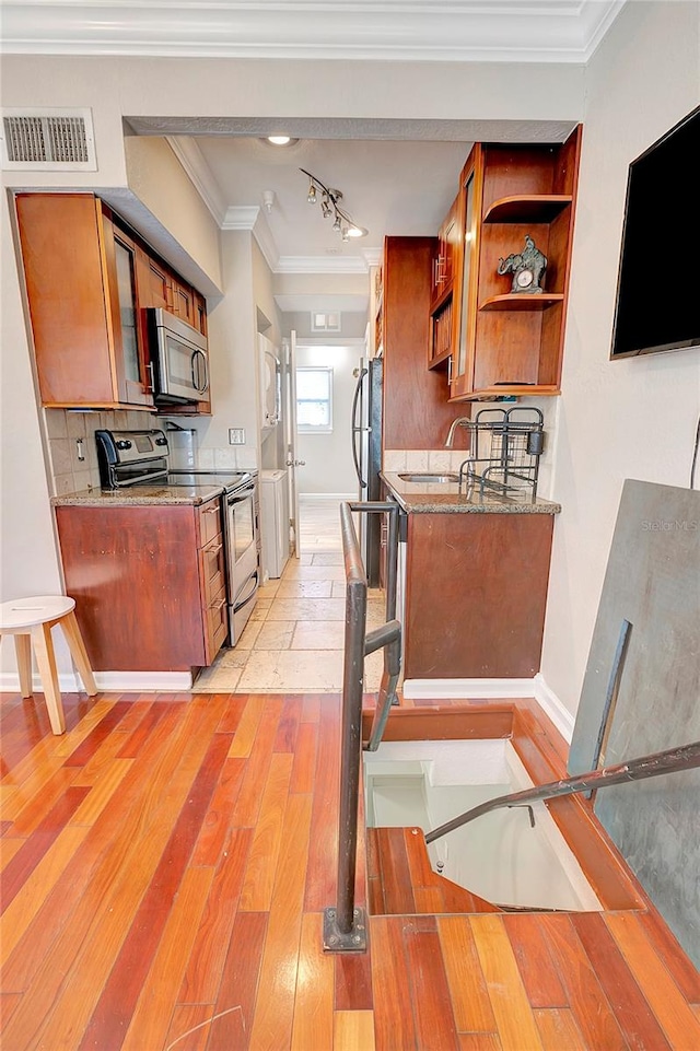 kitchen featuring light wood-type flooring, stone counters, backsplash, appliances with stainless steel finishes, and crown molding