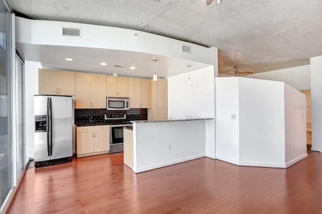 kitchen featuring kitchen peninsula, tasteful backsplash, stainless steel appliances, wood-type flooring, and decorative light fixtures