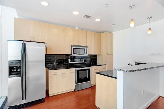 kitchen with kitchen peninsula, appliances with stainless steel finishes, light brown cabinets, hardwood / wood-style floors, and hanging light fixtures