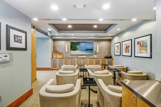 home theater featuring a raised ceiling, a barn door, and light colored carpet