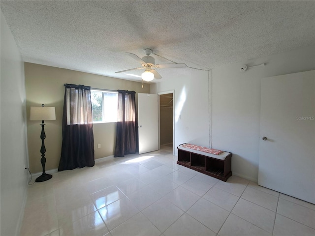 empty room featuring a textured ceiling, light tile patterned floors, and ceiling fan