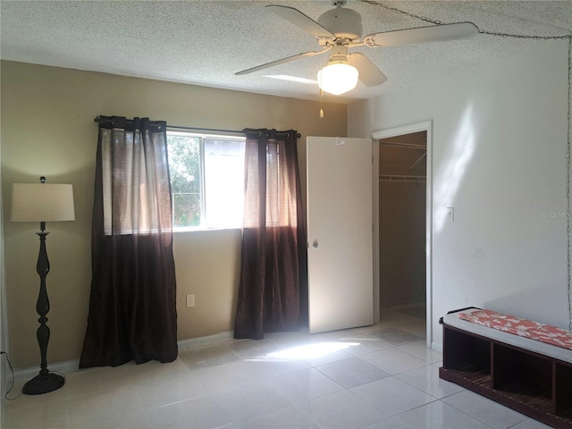 unfurnished bedroom featuring light tile patterned floors, a closet, a textured ceiling, ceiling fan, and a walk in closet