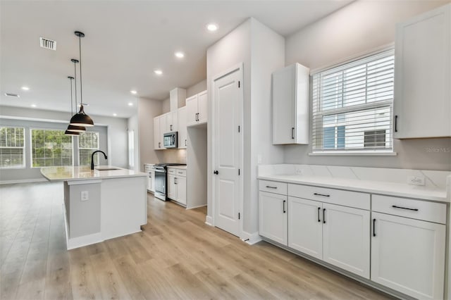 kitchen featuring decorative light fixtures, white cabinetry, stainless steel appliances, and an island with sink