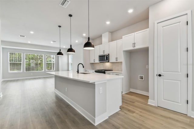 kitchen featuring sink, an island with sink, pendant lighting, white cabinets, and light wood-type flooring