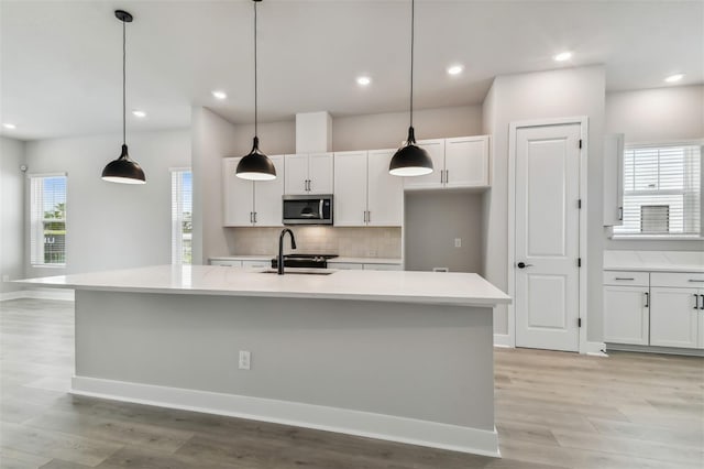 kitchen featuring a center island with sink, pendant lighting, white cabinetry, and black electric range