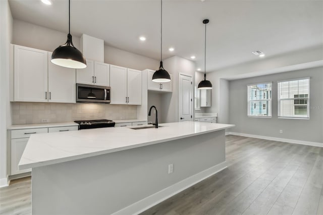 kitchen featuring light stone countertops, a center island with sink, white cabinetry, and sink