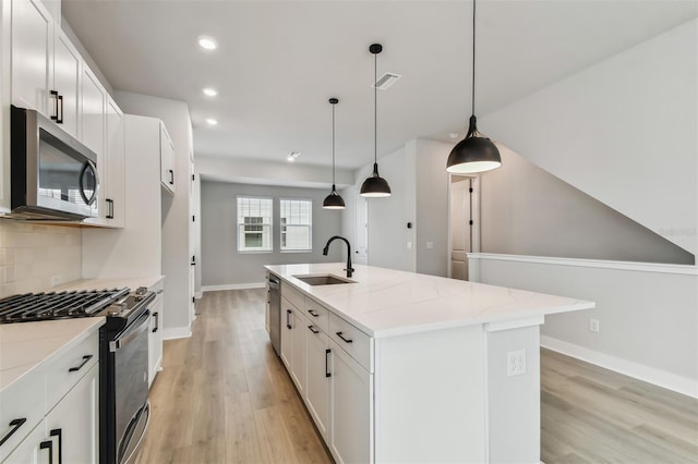 kitchen with a kitchen island with sink, sink, appliances with stainless steel finishes, decorative light fixtures, and light stone counters